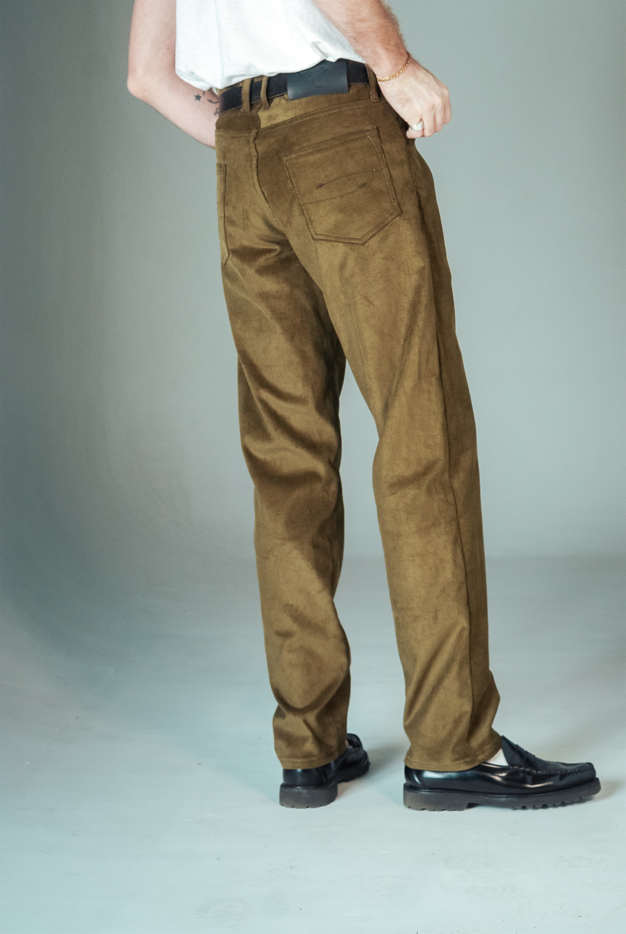Person wearing brown pants and black shoes on a plain background
