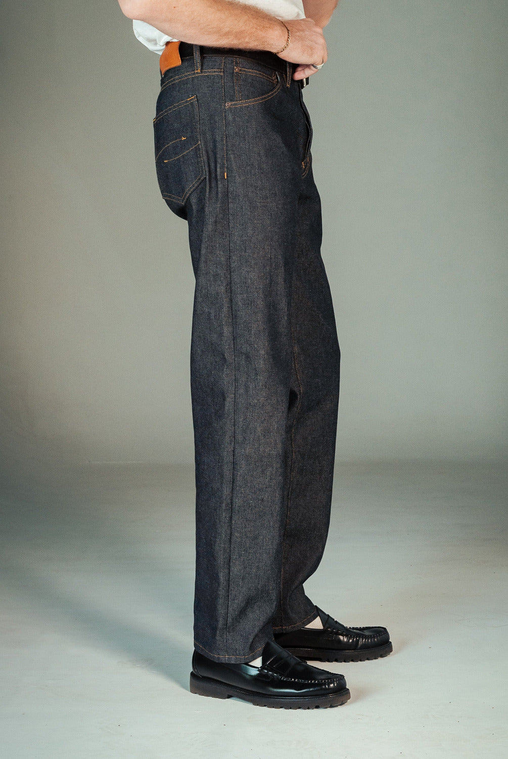 Person wearing dark denim jeans and black shoes on a plain background