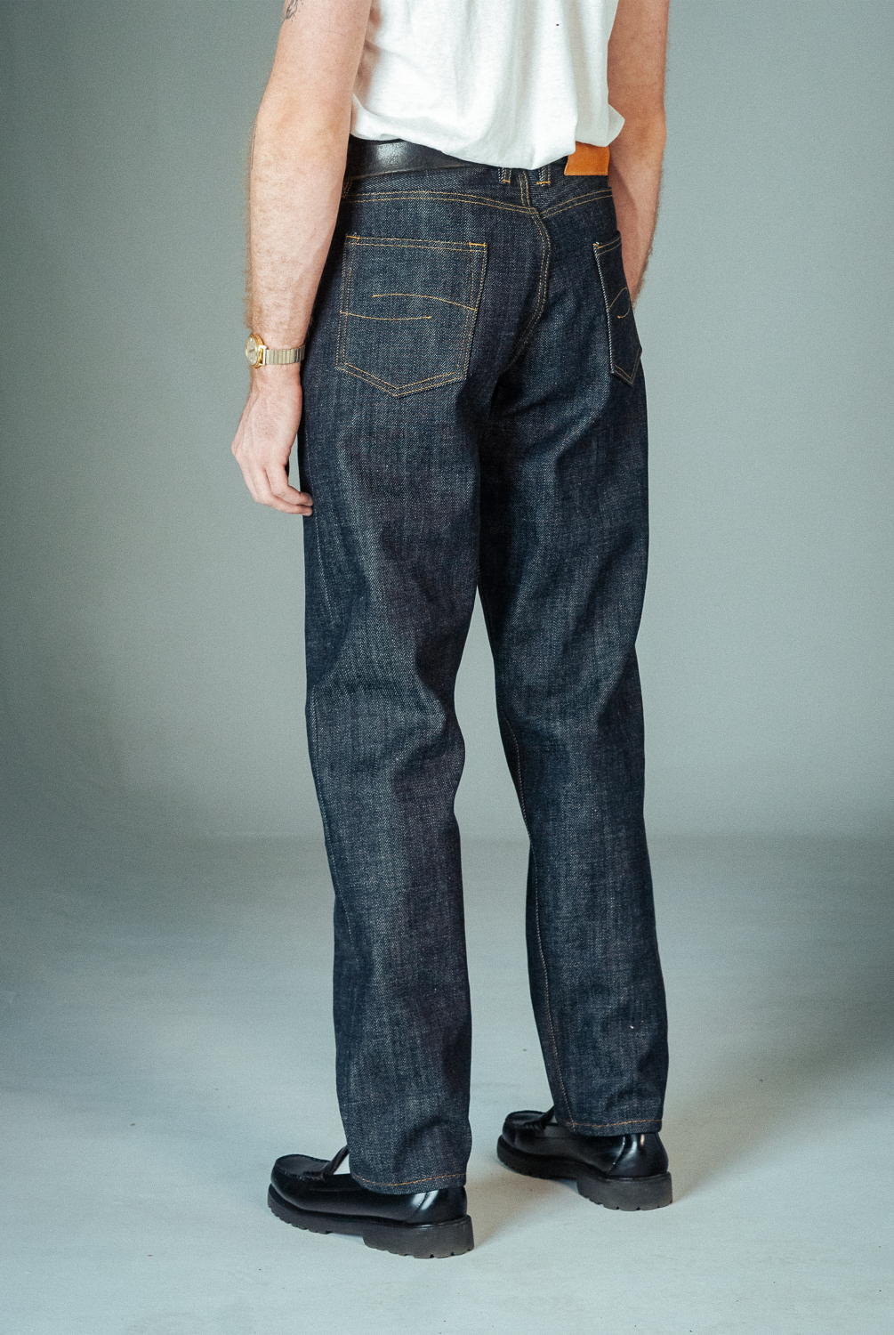 Person wearing dark blue jeans and black shoes on a plain background