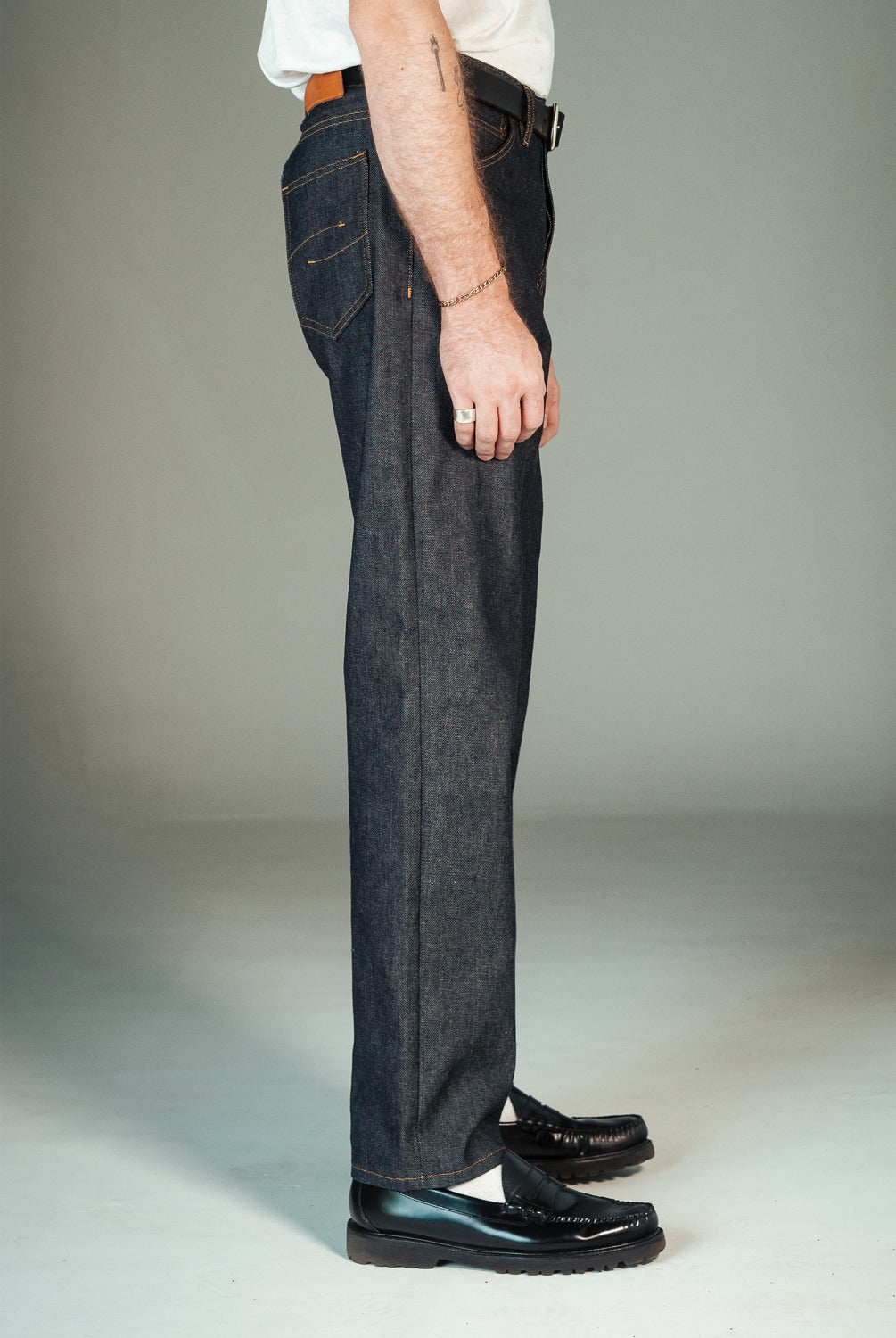 Person wearing dark blue jeans and black shoes on a plain background