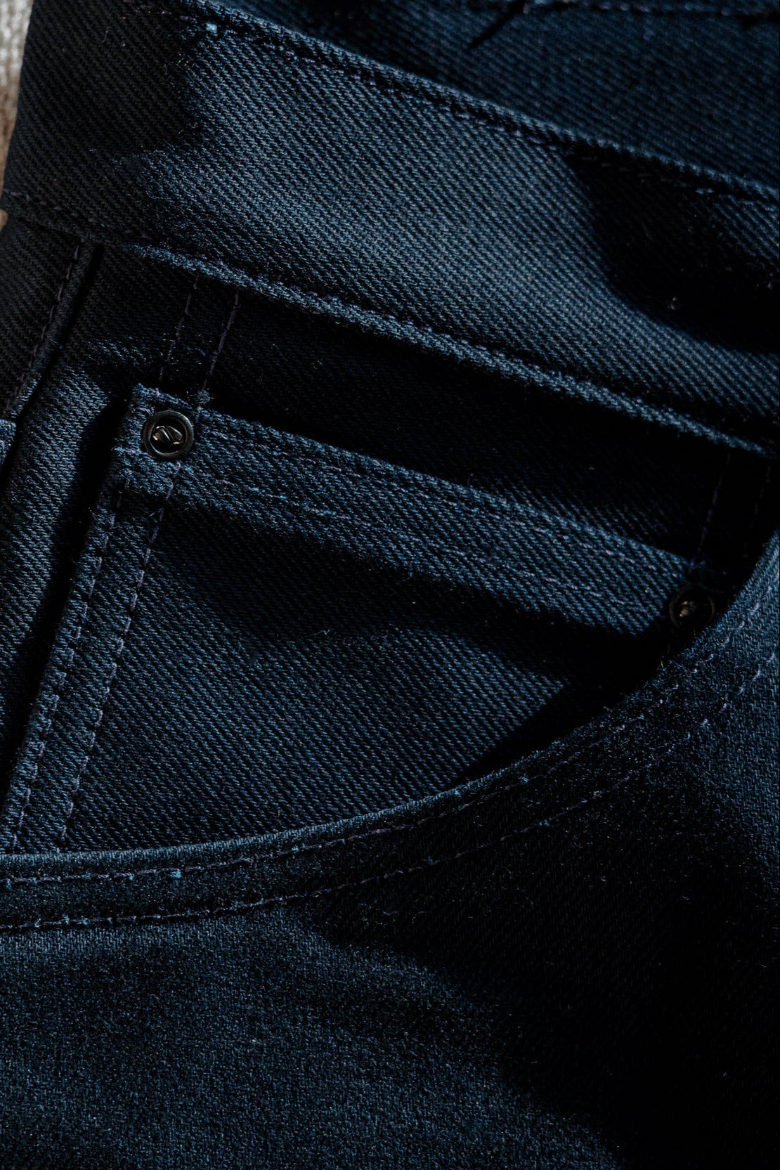Close-up of dark blue pants with a textured wall background