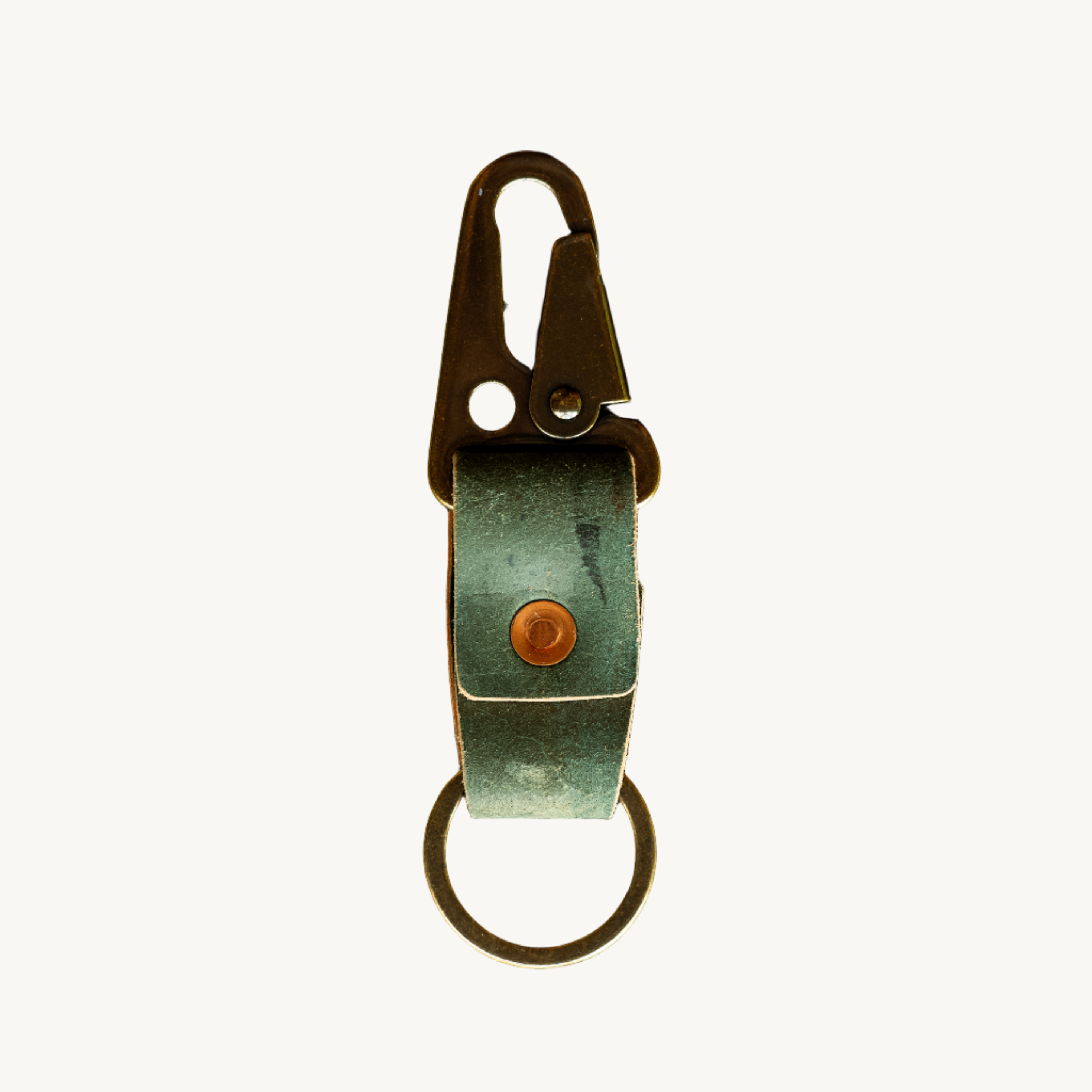 A black and brown key clip made of Horween shell cordovan with a brass hardware, including a lever clip and a keyring, placed on a textured background.