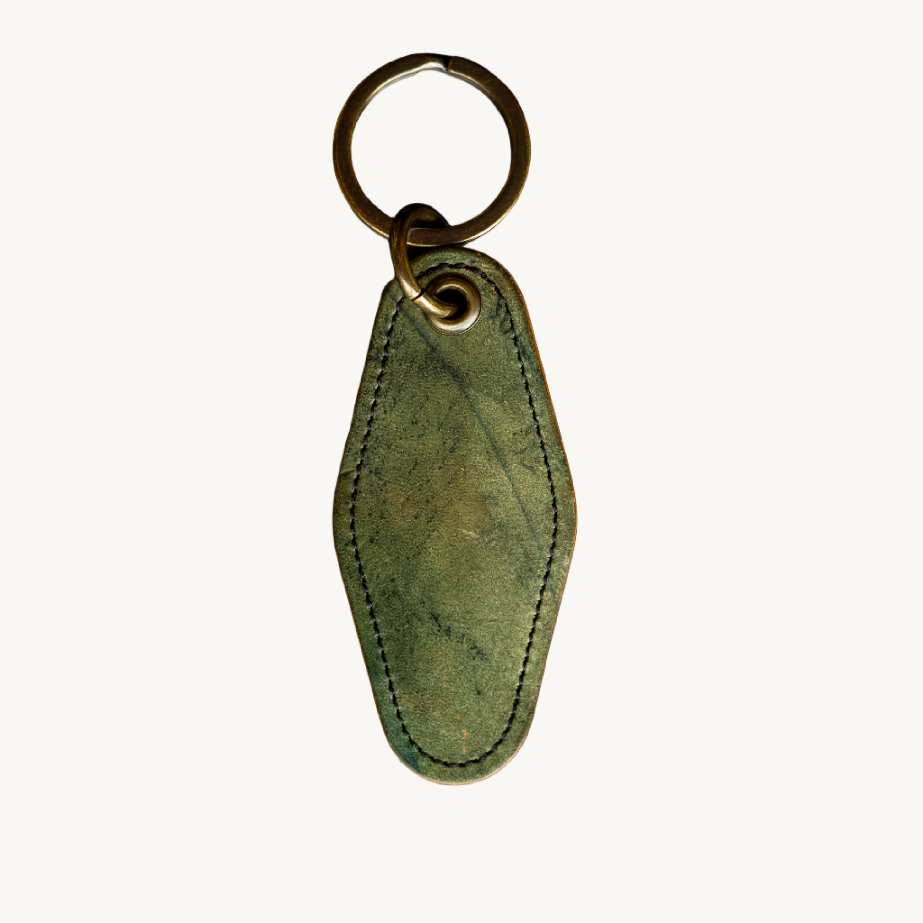 A green leather motel key ring with a brass keyring and split ring, hand-hammered brass grommet, on a dark textured background.