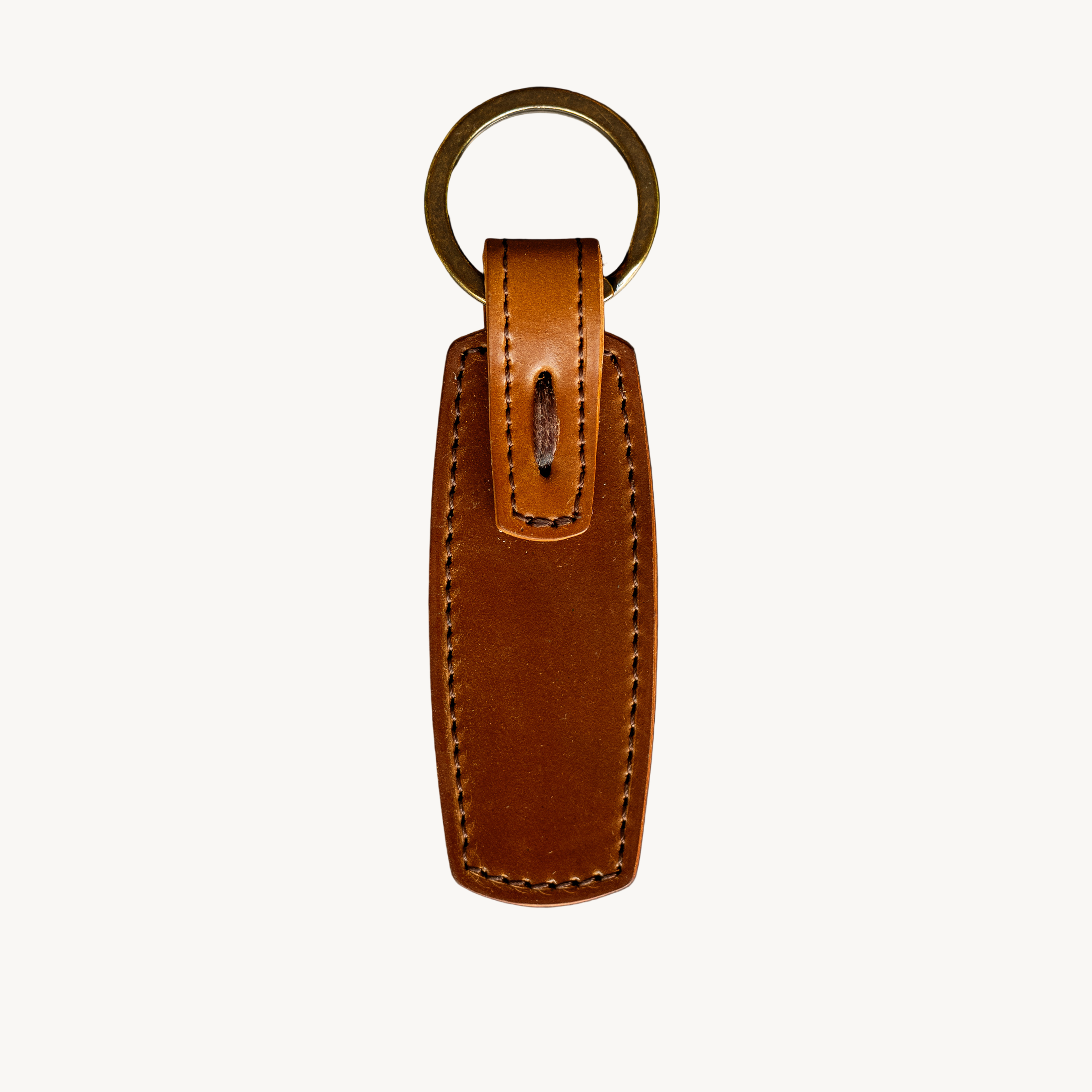 Brown leather key fob with gold ring on a gray surface