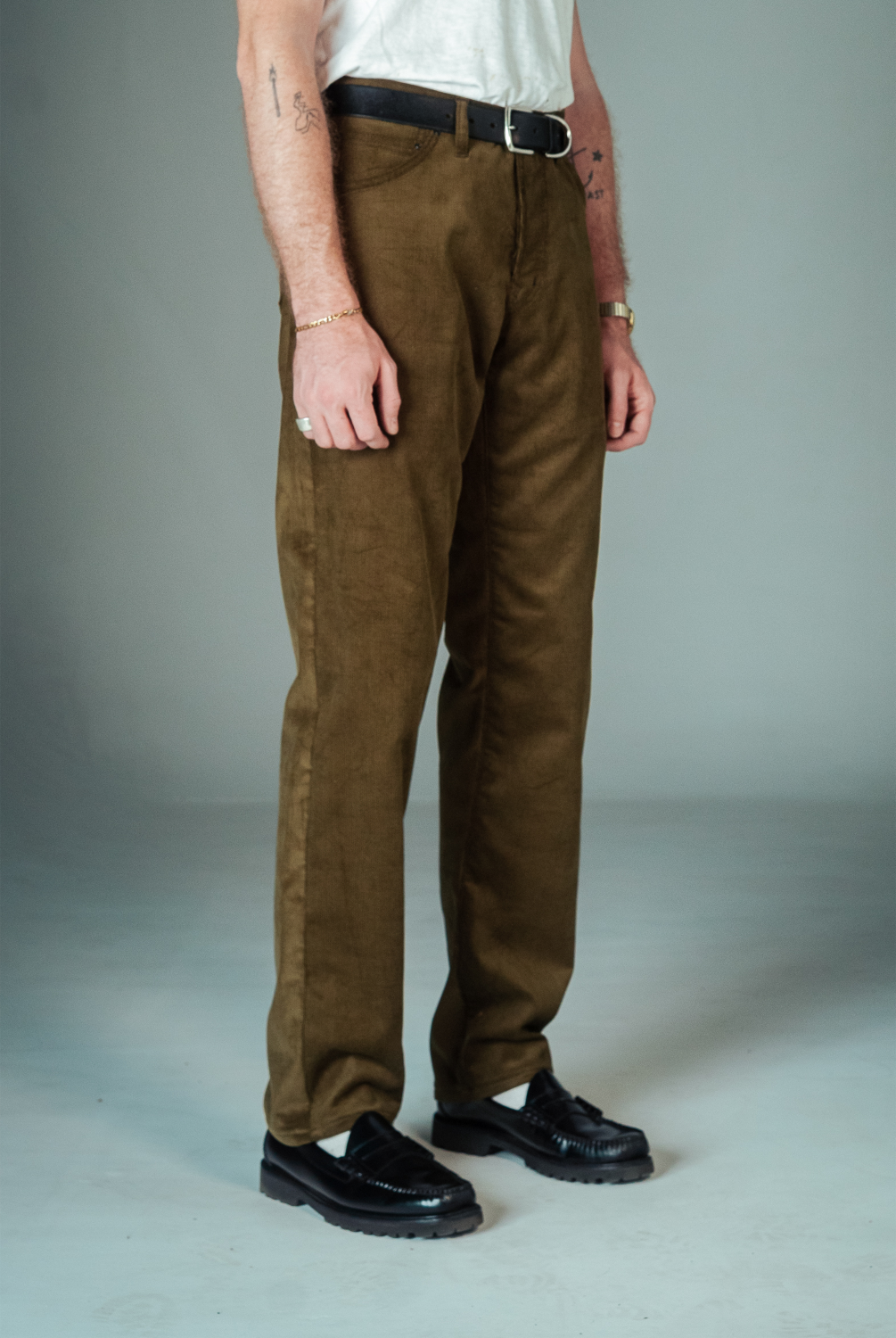 Person wearing brown pants and black shoes on a plain background