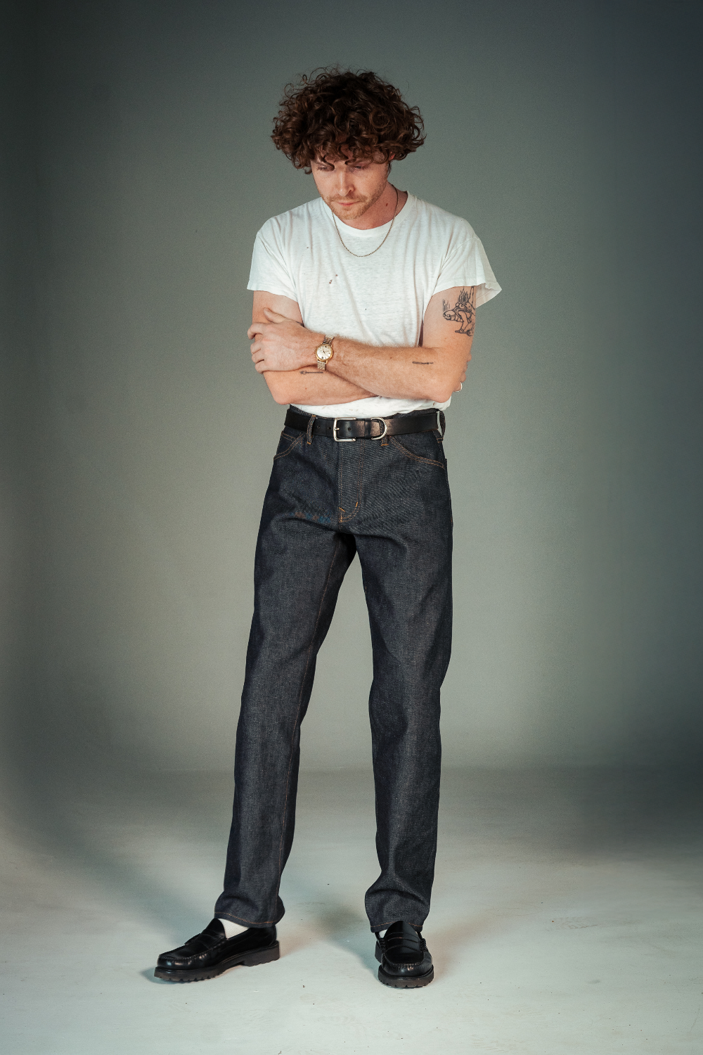 Man wearing a white t-shirt and dark jeans standing against a plain background